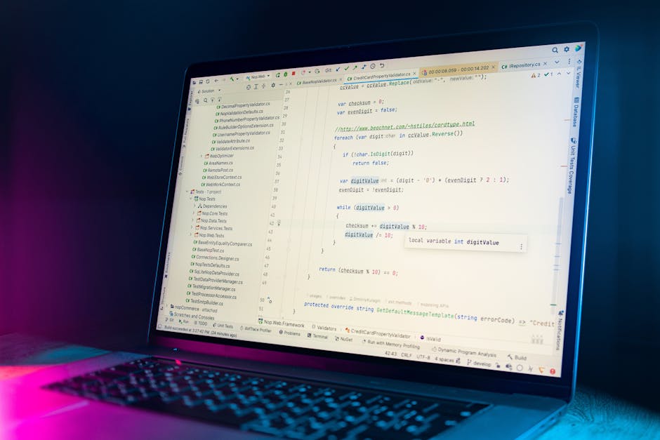 A close-up view of a laptop computer displaying lines of code on the screen, with a focus on programming syntax such as variables, functions, and comments. The laptop is situated on a desk with a dark